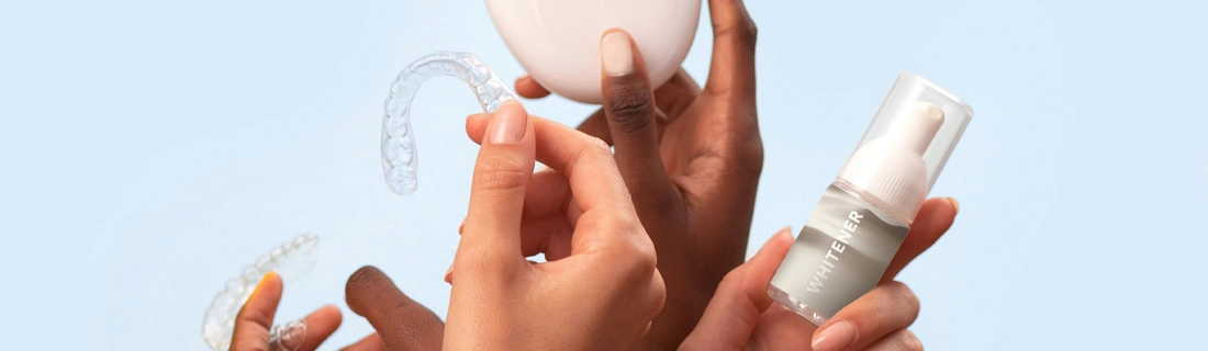 Hands holding clear aligners, a whitening bottle, and a round container against a light blue background.