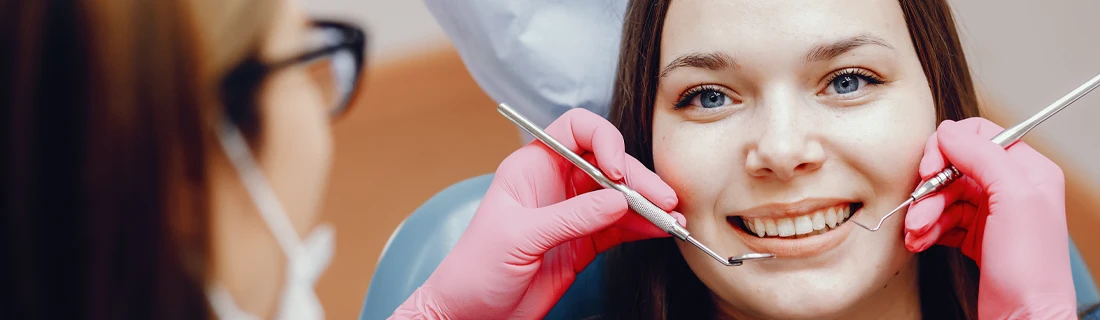 Dental professional holding dental instruments near a seated patient's teeth during an exam.