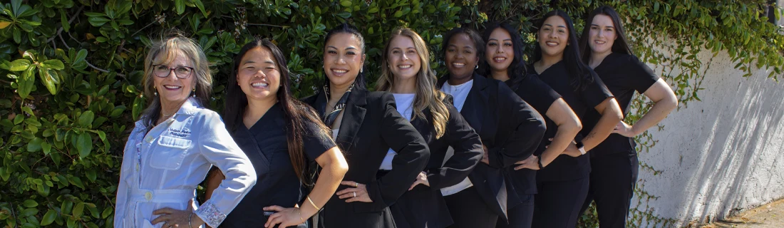 Dr. Melanie Parker and the clinic team standing outdoors in a line with hands on hips in front of a leafy hedge and wall.