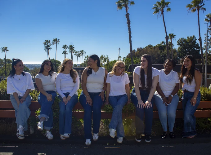 Dr. Melanie Parker with the staff sitting outdoors on a bench with palm trees and a clear blue sky in the background.