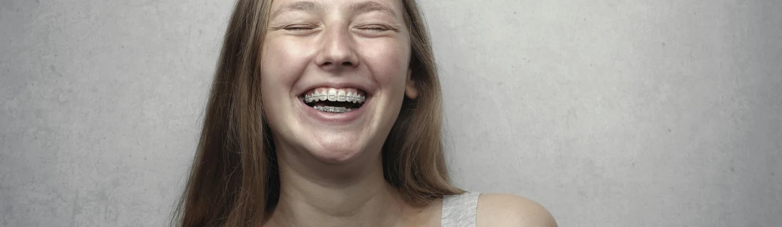 Person with braces smiling against a light gray background, shown from the shoulders up.